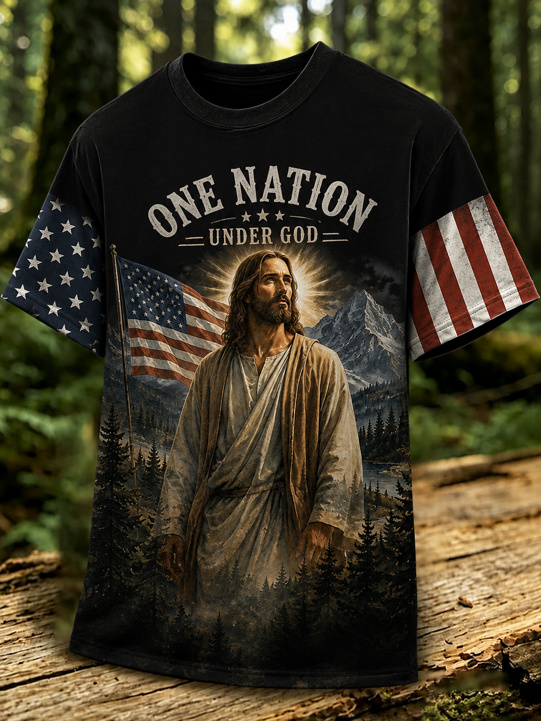 A black graphic t-shirt featuring a printed design of Jesus standing in a forest with mountains and an American flag, with the text 'ONE NATION UNDER GOD' across the chest. The shirt is displayed on a wooden log with a blurred forest background.